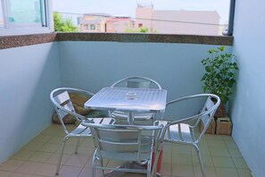 Un petit balcon avec une table et des chaises en métal, un pot de fleurs et une vue sur les bâtiments en arrière-plan.