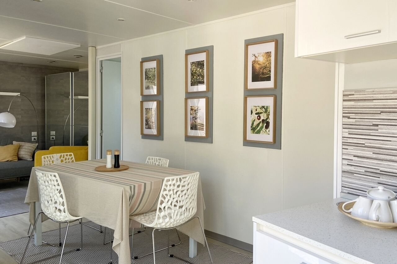 Un espace de salle à manger moderne, avec une table dressée pour quatre personnes, entourée de chaises blanches ornées de motifs ajourés complexes.