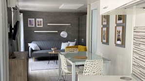 A modern living room with a sofa, a glass dining table, and a TV. - Ulika Rovinj Camping (Rovinj)