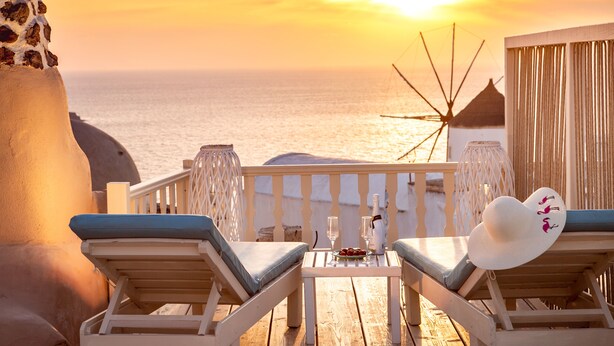 A wooden deck with two lounge chairs, a small table with a bottle and glasses, and a decorative hat. - Thetis Cave Houses (Santorini)