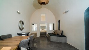 A modern interior with a wooden dining table, cushioned chairs, a bench, and a small kitchenette in the background. - Thetis Cave Houses (Santorini)