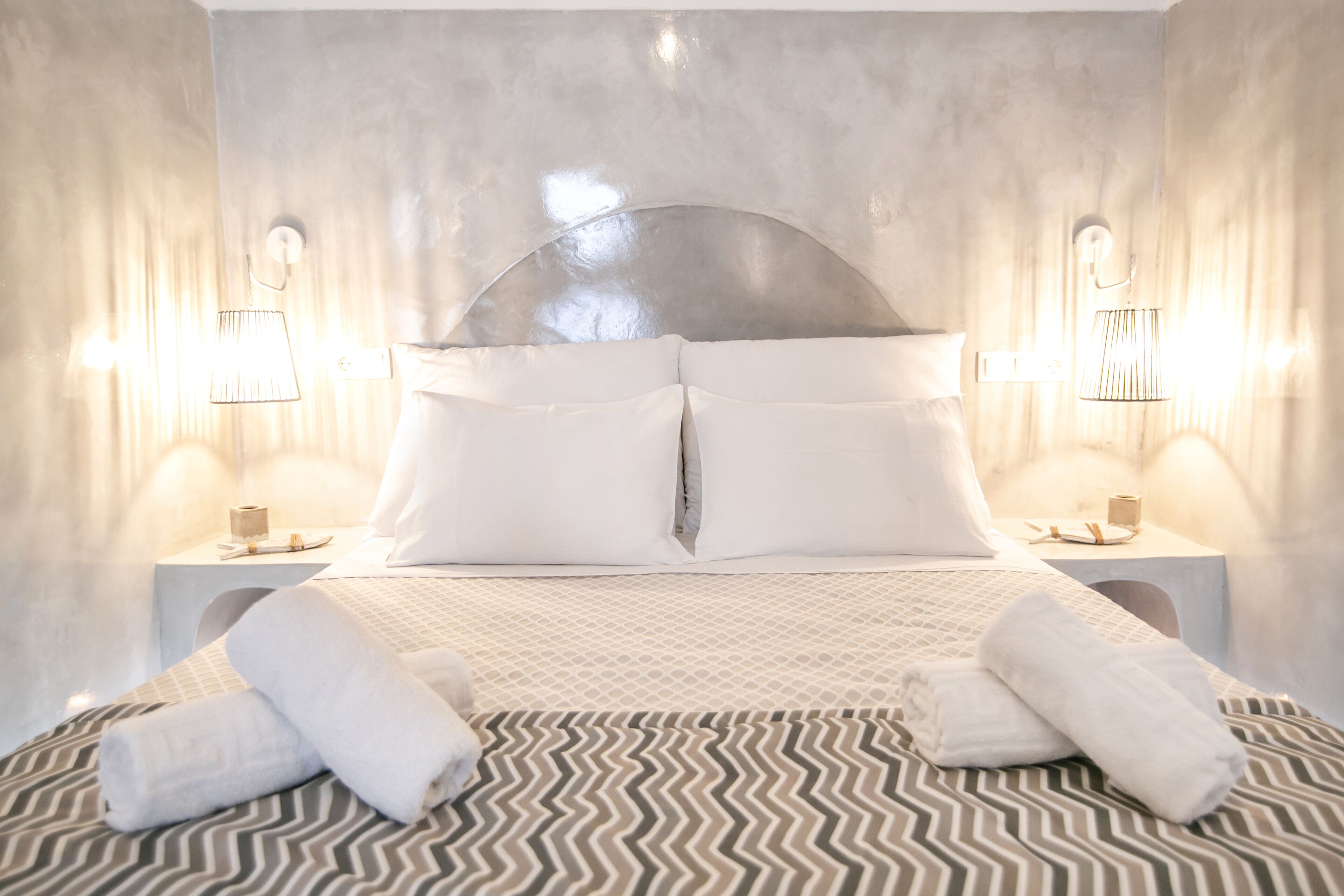 A hotel room with a large bed, two bedside tables, and wall-mounted lamps.