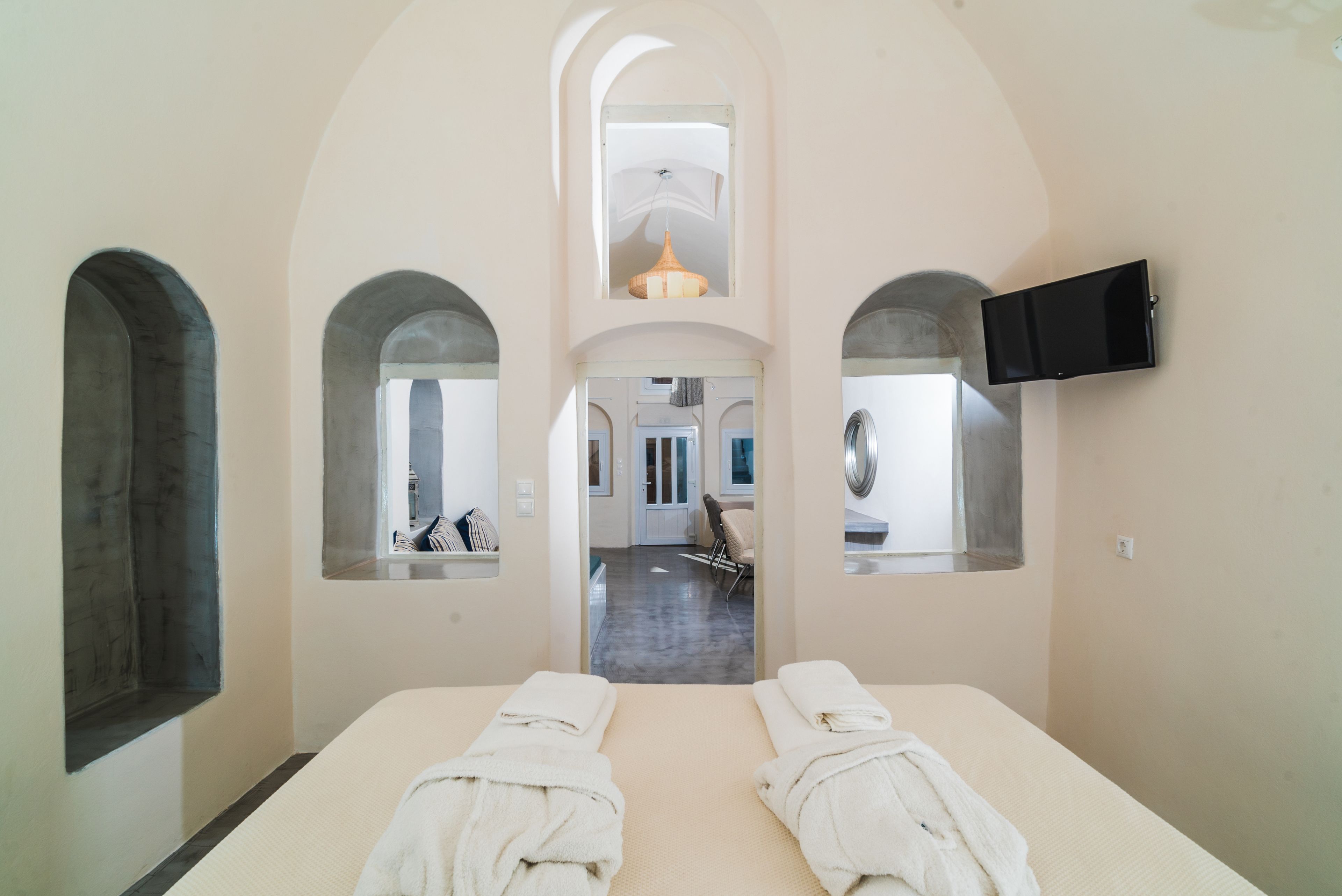 Une chambre d’hôtel avec deux lits, un téléviseur fixé au mur et une vue sur le couloir et une autre chambre, grâce à une fenêtre en arc de cercle.