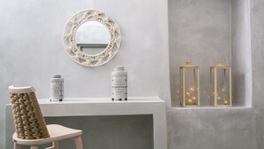 A bathroom with a white vanity, a round mirror, two patterned vases, and two hanging lanterns. - Thetis Cave Houses (Santorini)
