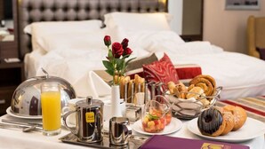 A hotel room with a neatly made breakfast table, a bed with white linens, and a decorative vase with red flowers. - The Envoy Hotel (Abuja)