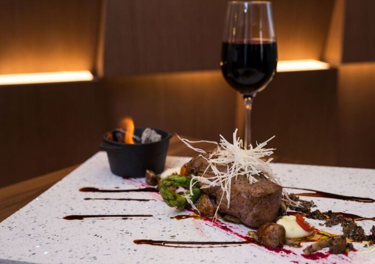 Un plat présenté sur une assiette, accompagné d’un verre de vin rouge, d’asperges et d’un petit ramequin de sauce.