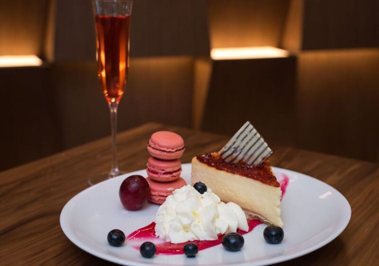 A dessert plate with macarons, whipped cream, and a slice of cheesecake on a white plate.