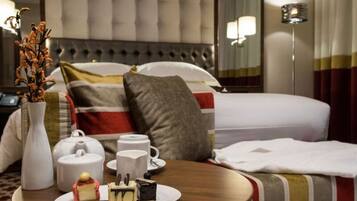 Una habitación de hotel con una cama, una mesita de noche con un jarrón, tetera, tazas y un plato de pastel.