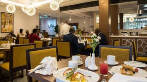 A hotel dining area with round tables, yellow chairs, and hanging crystal chandeliers. - The Envoy Hotel (Abuja)