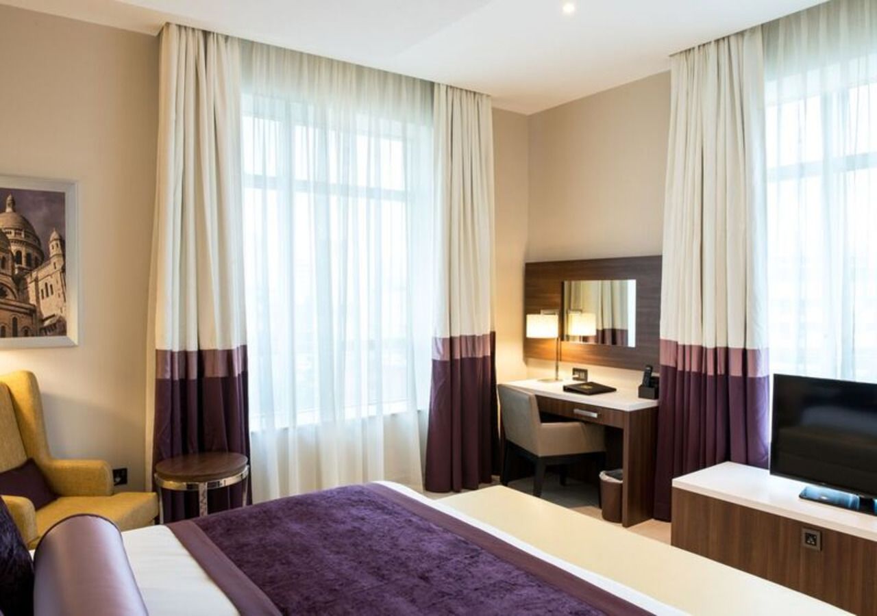 A hotel room with a bed, a desk, a chair, a television, and curtains.