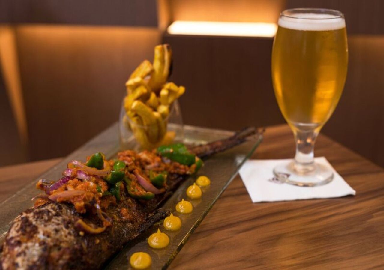 Un poisson grillé, garni de divers accompagnements, et un verre de bière, le tout posé sur une table en bois.