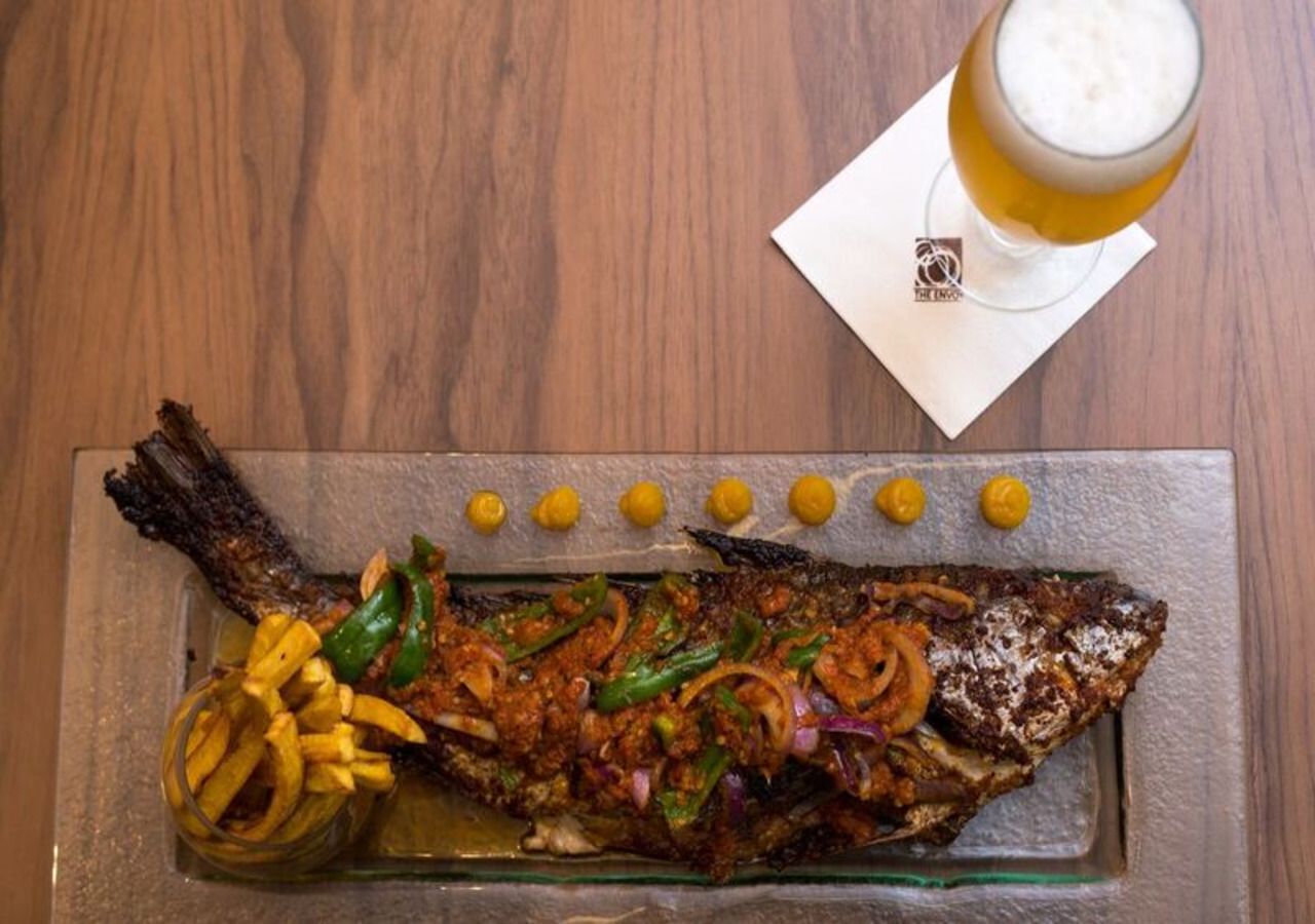 Gegrilde vis met groenten en een glas bier op een houten tafel.