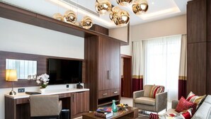 A modern living room with a flat-screen TV, a wooden desk, a comfortable sofa, and a coffee table. - The Envoy Hotel (Abuja)
