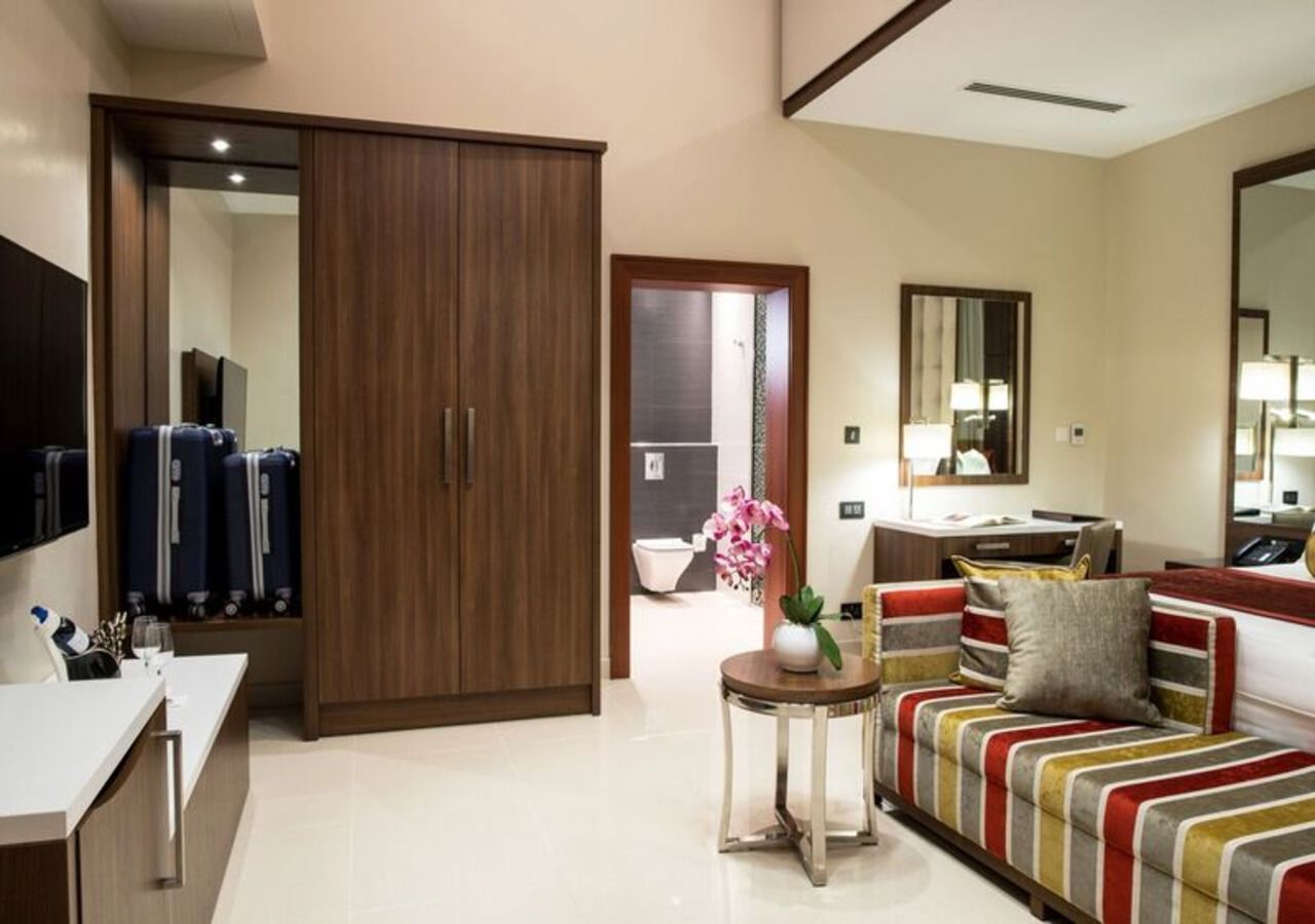 A modern hotel room with a large wardrobe, a sofa, a small table with a vase, and a mirror.