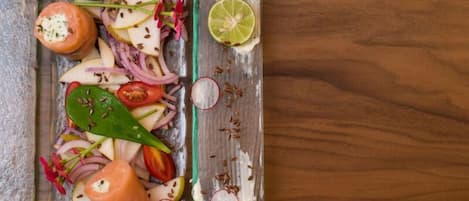 Una mesa de madera con un recipiente de vidrio que contiene una ensalada de tomates, cebollas, rábanos y una rodaja de lima.