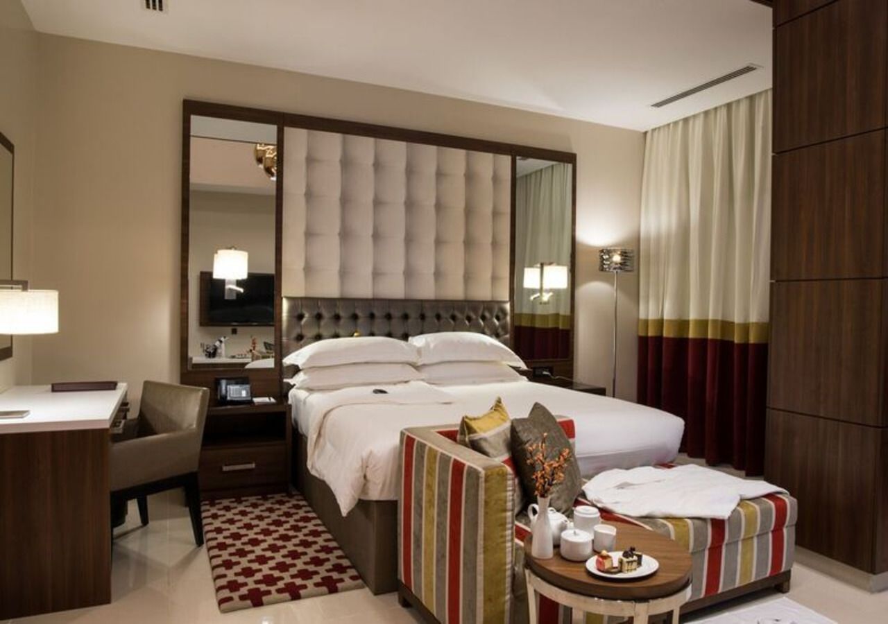 Une chambre d’hôtel avec un grand lit, un bureau, une chaise, une table de chevet avec une lampe et un miroir.