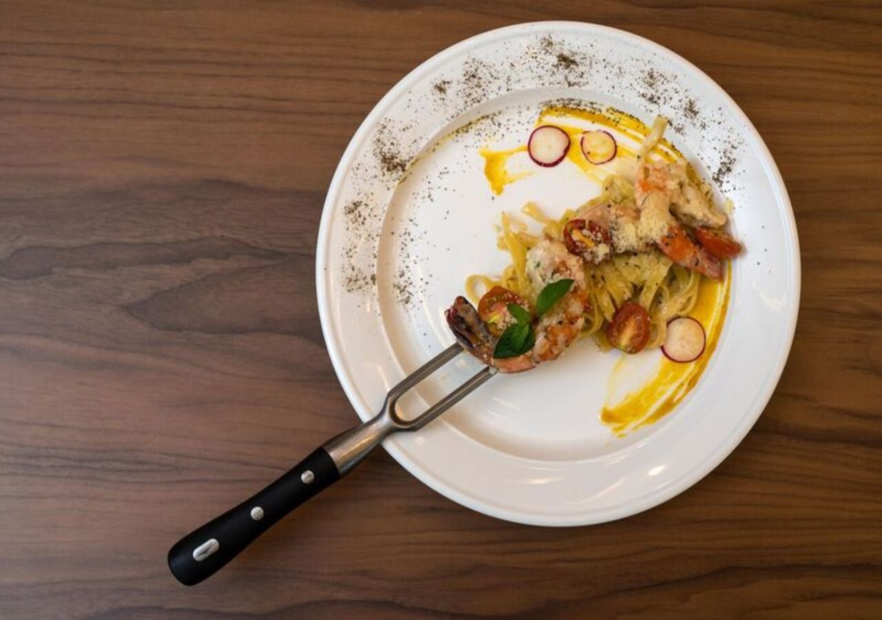 A white plate with remnants of food, including shrimp and vegetables, on a wooden table.