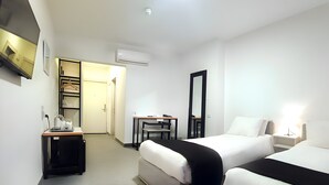 A hotel room with two beds, a desk, a chair, a TV, and an air conditioning unit. - Nomads Hotel - Hostel (Amman)