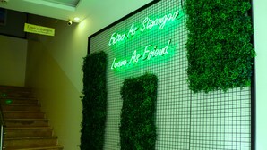 A staircase with a neon sign that reads "Enter as stranger, leave as friend" and green foliage on the wall. - Nomads Hotel - Hostel (Amman)