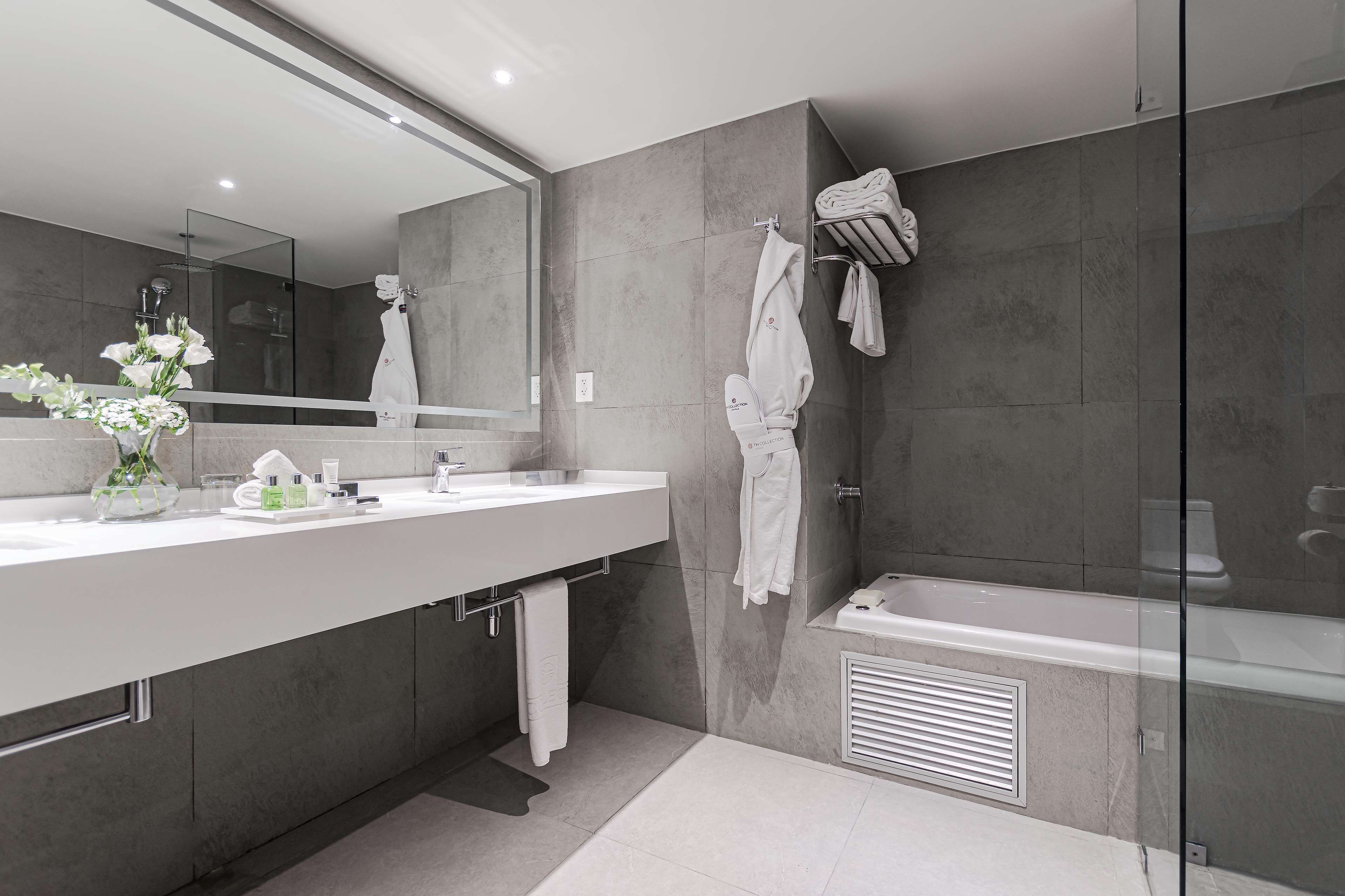 A modern bathroom with a large mirror, two sinks, a bathtub, and a glass shower enclosure.