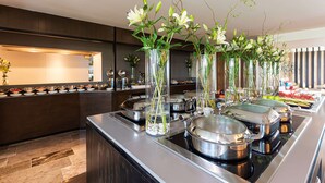 A buffet setup with multiple serving stations, glass vases with flowers, and stainless steel serving dishes. - NH Collection Merida Paseo Montejo (Mérida)