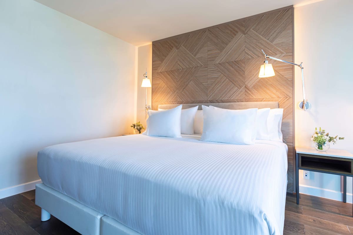 A modern hotel room with a large bed, a wooden accent wall, and two bedside lamps.