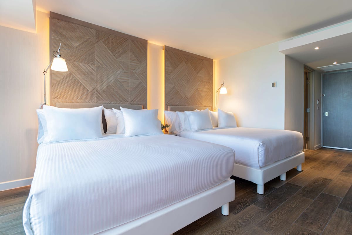 A hotel room with two beds, a wooden accent wall, and a door leading to a hallway.