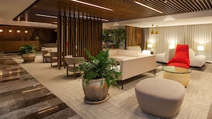 A modern lobby with a sofa, chairs, a coffee table, and potted plants. - NH Collection Merida Paseo Montejo (Mérida)