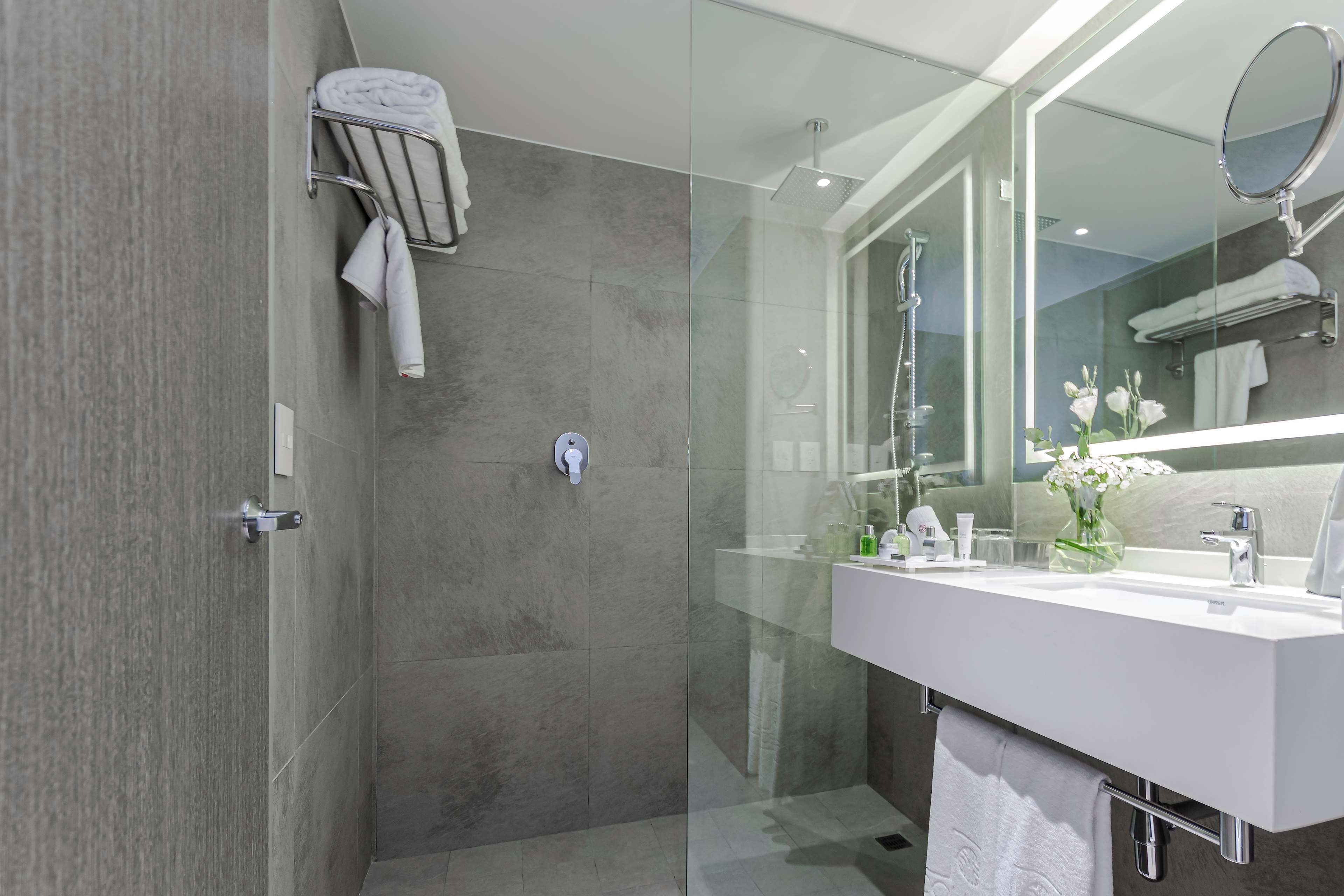 A modern bathroom with a glass shower enclosure, a white vanity with a mirror, and a towel rack.