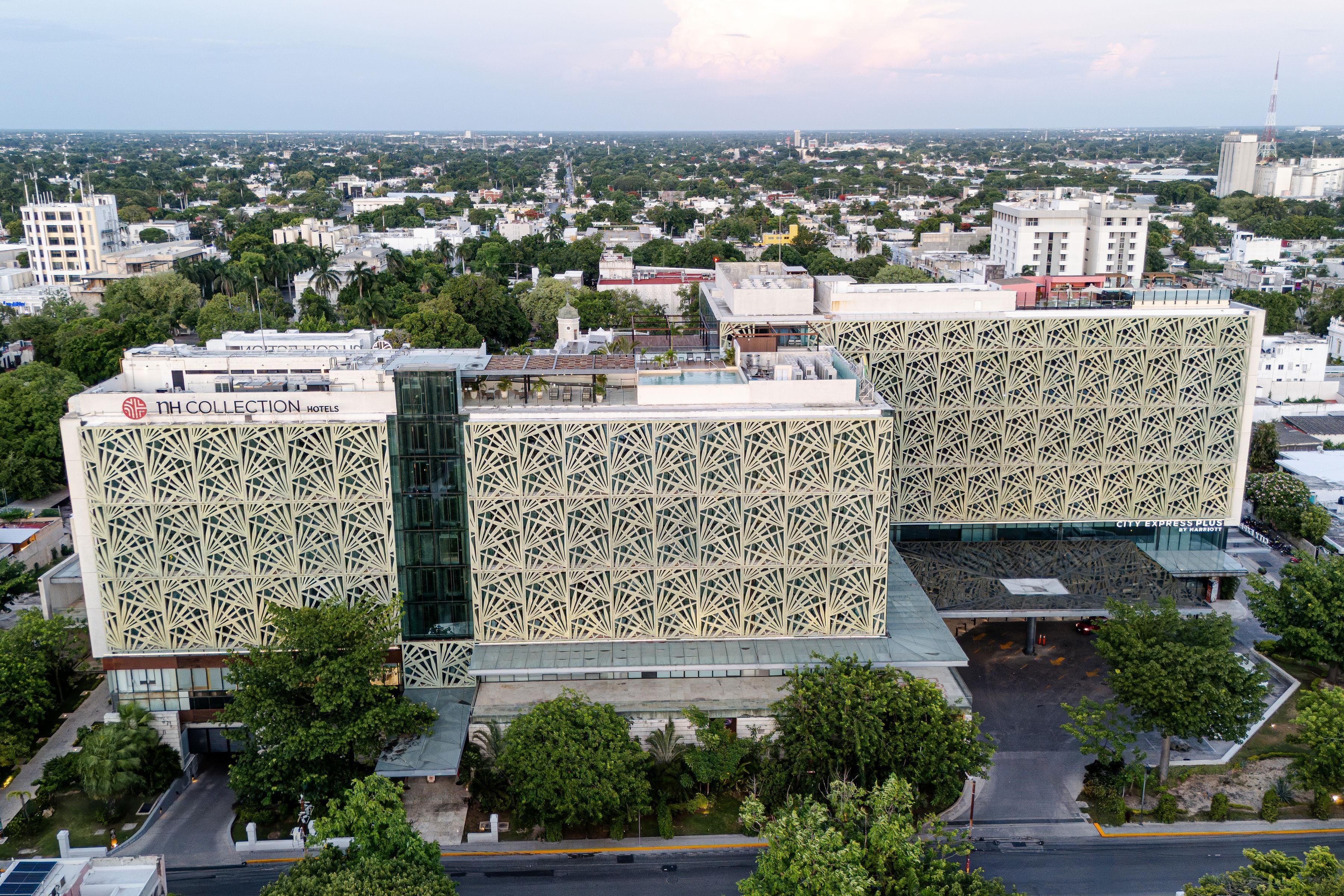 Un hotel moderno con una fachada geométrica distintiva, situado en un entorno urbano rodeado de edificios y vegetación.