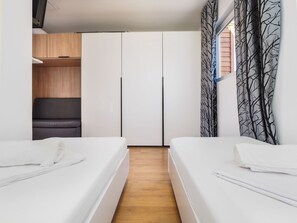 A modern bedroom with two single beds, a wooden floor, a wardrobe, and a window with a tree pattern curtain. - Mediteran Travel Camping Sveti Križ (Trogir)