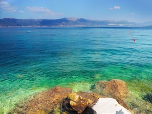 A clear coastal view with rocky formations and a distant cityscape. - Mediteran Travel Camping Sveti Križ (Trogir)
