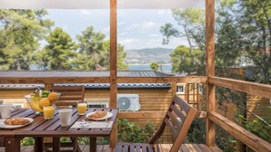 Une terrasse en bois avec une table dressée pour le petit-déjeuner, offrant une vue panoramique sur des arbres et une étendue d’eau.