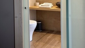 Un baño con inodoro, lavamanos, espejo y perchero para toallas.