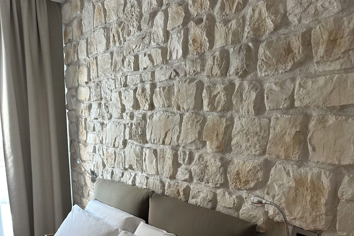 Ein Schlafzimmer mit Steinsturz, einem Bett mit weißer Bettwäsche, einem Nachttisch mit Lampe und einem Buch.