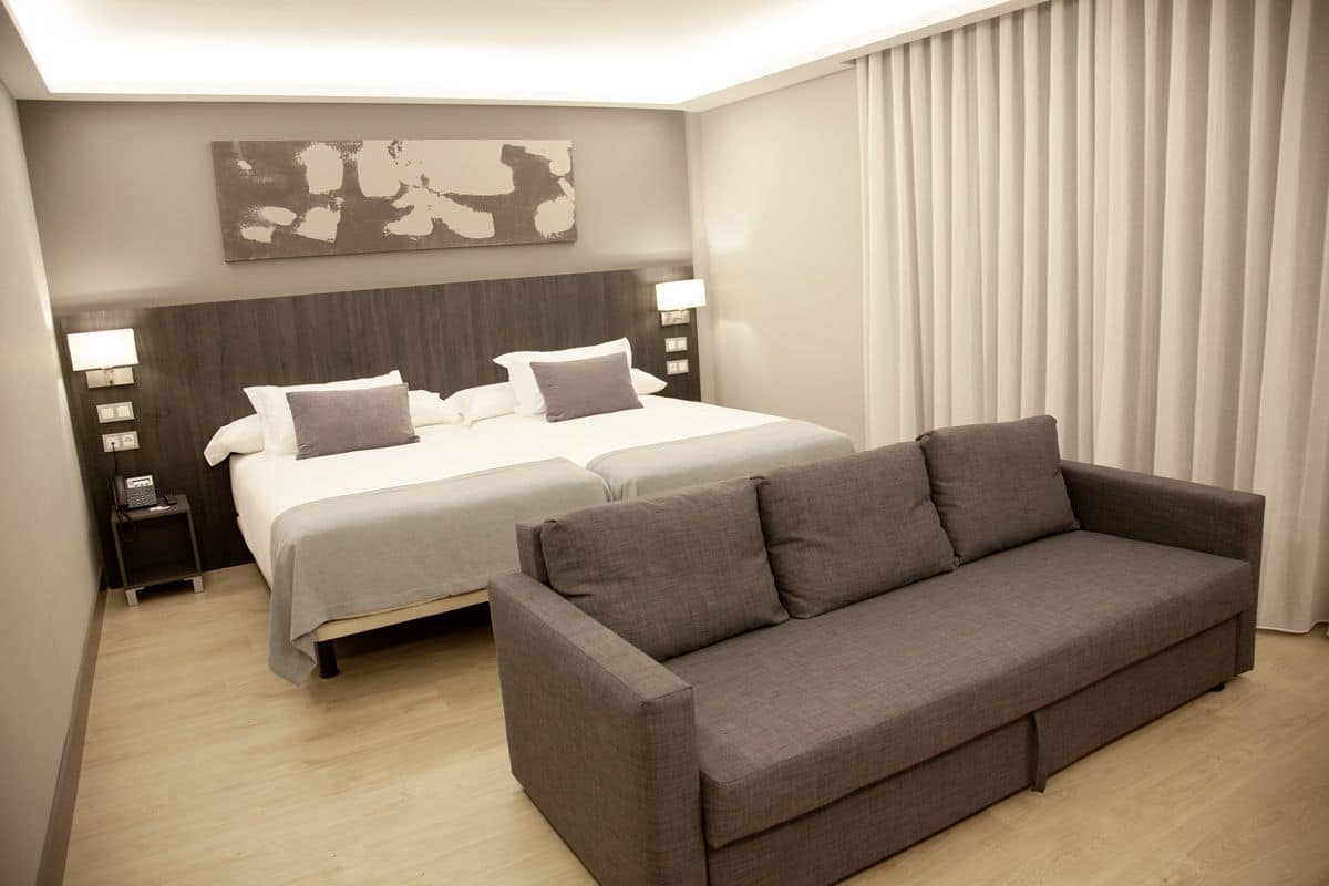 Habitación de hotel con una cama grande, un sofá, una mesita de noche con lámpara y una obra de arte colgada en la pared.