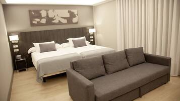 Habitació d'hotel amb un llit gran, un sofà, una tauleta de nit amb una làmpada i una obra d'art penjada a la paret.