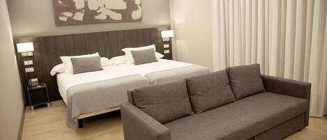 Habitación de hotel con una cama grande, un sofá, una mesita de noche con lámpara y una obra de arte colgada en la pared.