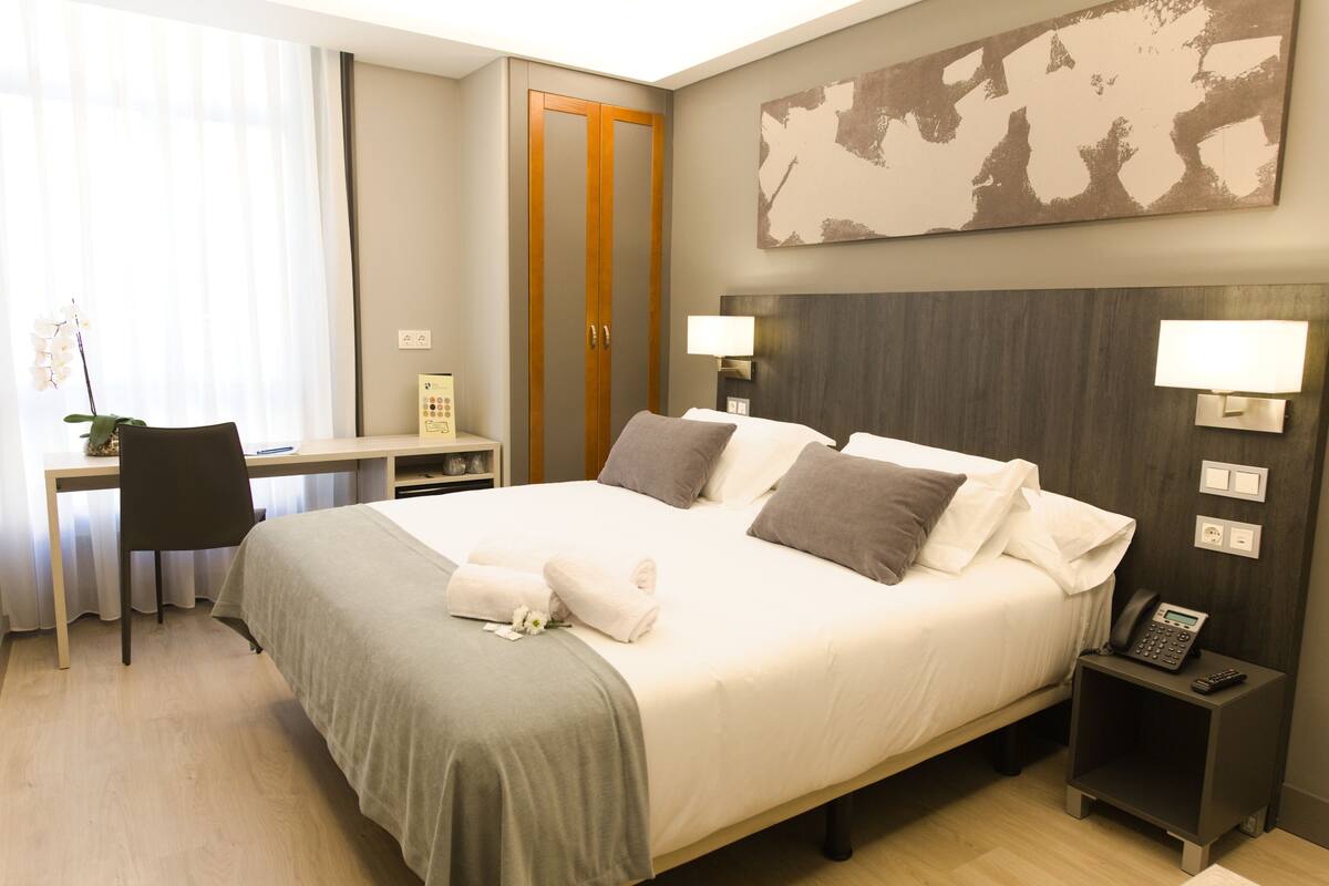 Habitación de hotel con cama, escritorio, silla y mesita de noche con teléfono.