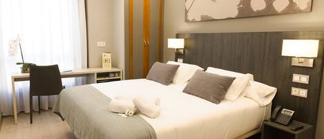 Een hotelkamer met een bed, bureau, stoel en nachtkastje met een telefoon.