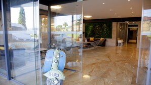 Een moderne lobby met een klassieke scooter, glazen deuren, een groene wand en een zithoek.