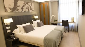 A hotel room with two beds, a desk, a chair, a nightstand with a phone, and a painting on the wall.