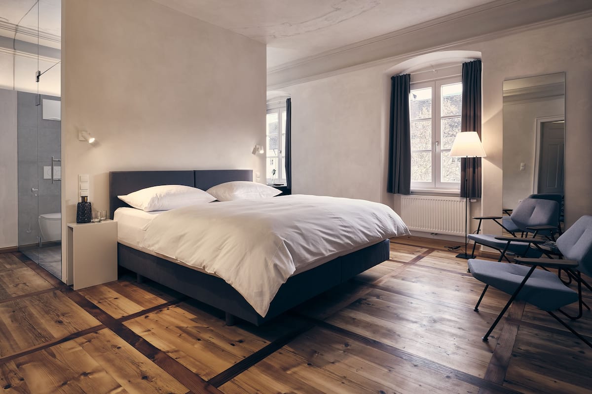 Ein modernes Schlafzimmer mit einem großen Bett, einem Nachttisch, einem Sessel und einem Fenster mit Vorhängen.