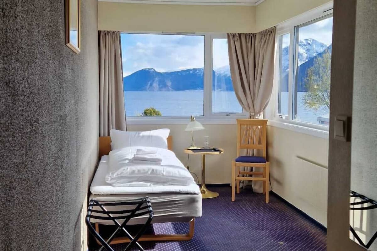 Habitación de hotel con cama, una silla, una mesita y ventana con vista a la montaña.