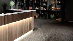 A modern reception area with a wooden reception desk, black shelving units, and a patterned carpet. - Sognefjord Hotel (Sogndal)