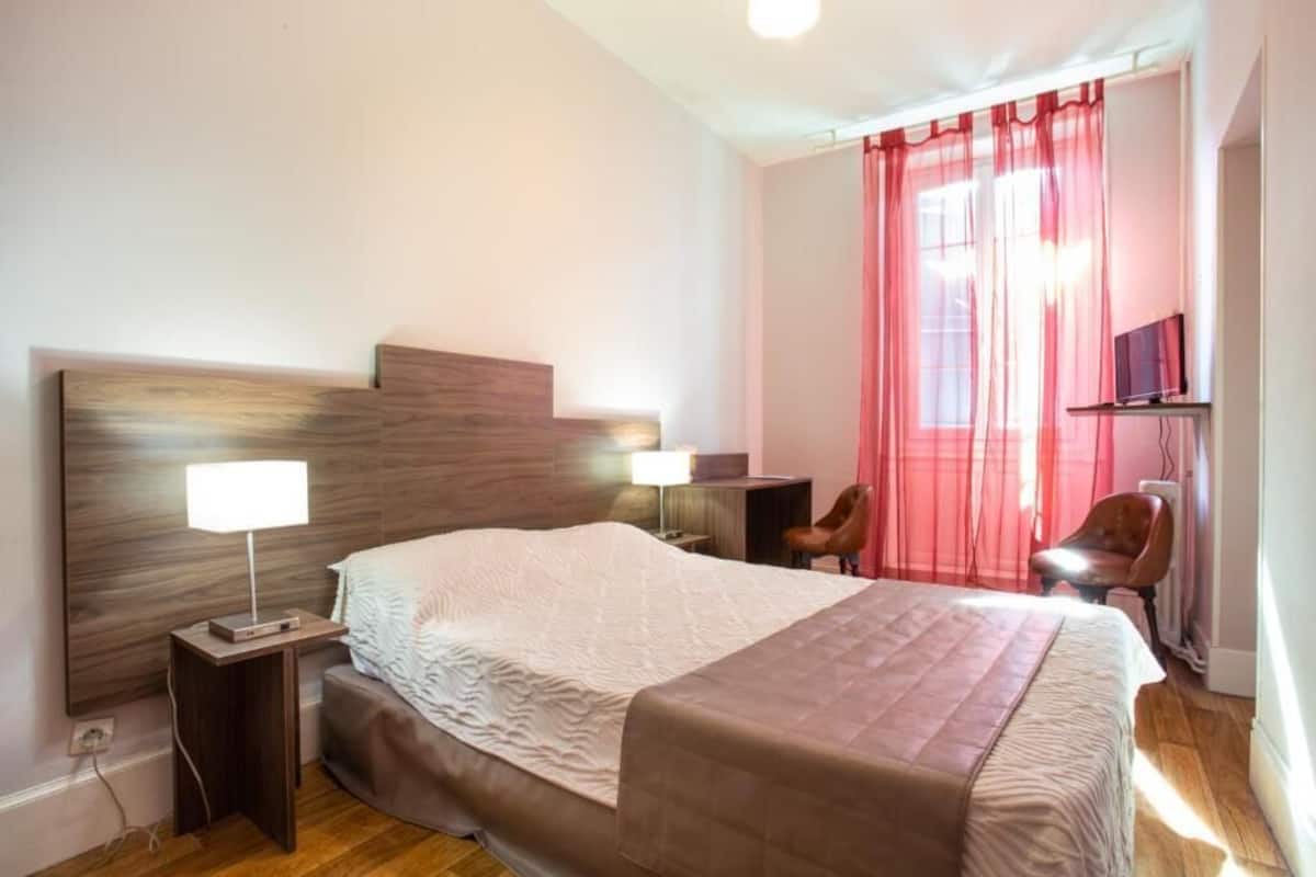 A hotel room with a bed, bedside table with lamp, chair, and TV.