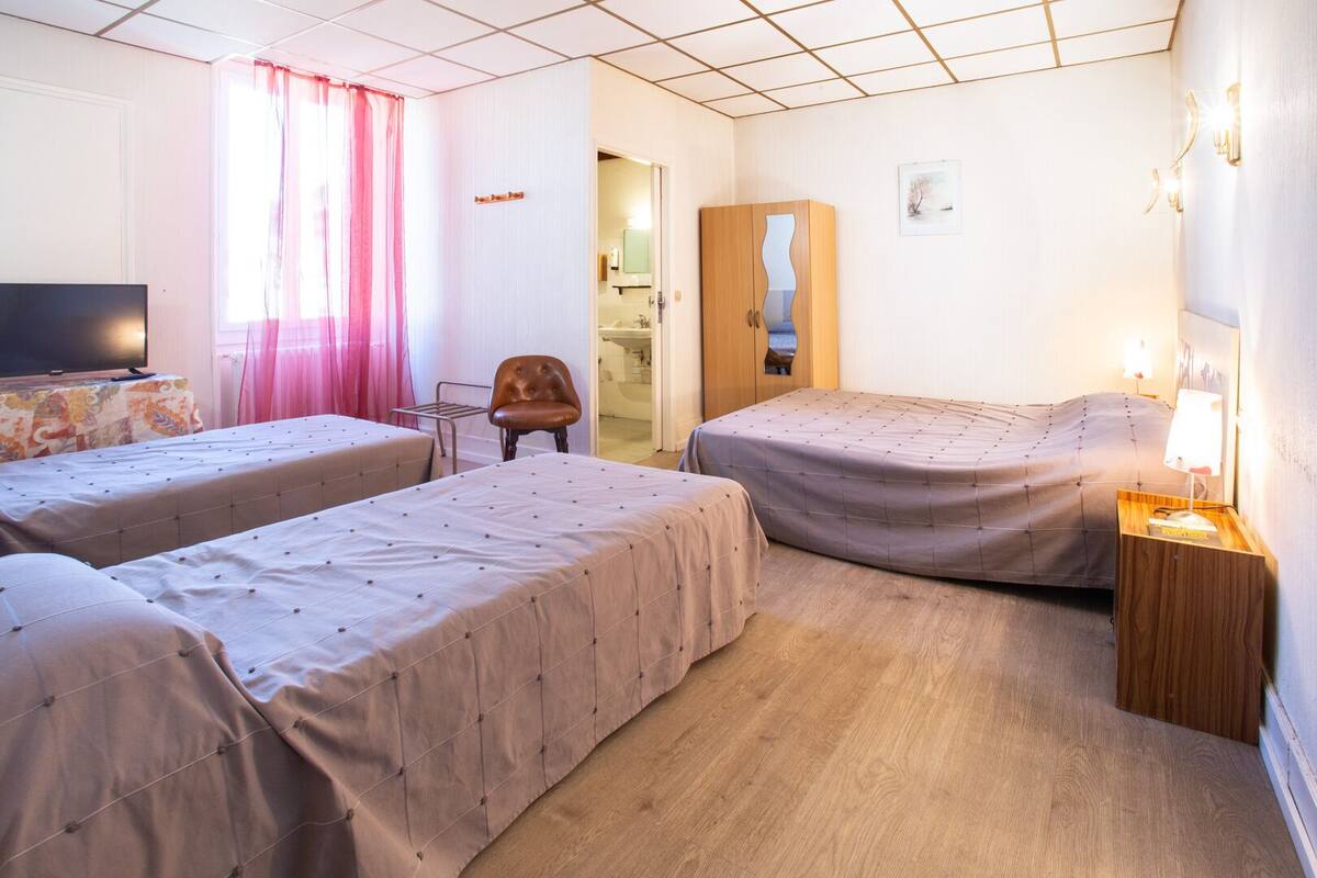 A hotel room with two beds, a television, a chair, and a wooden cabinet.