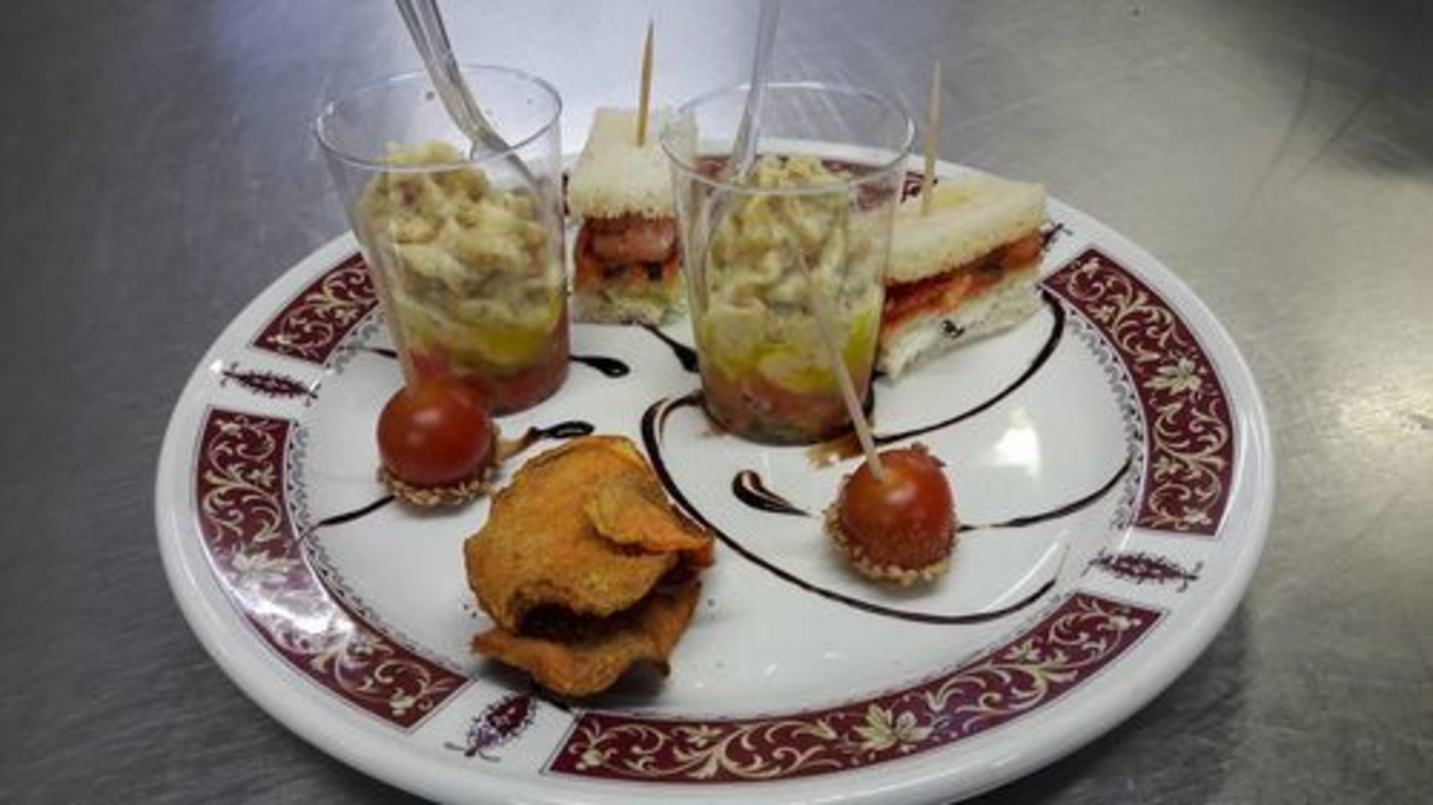 Un plato con un sándwich, dos vasos de una bebida en capas y un pequeño objeto redondo con una cereza encima.