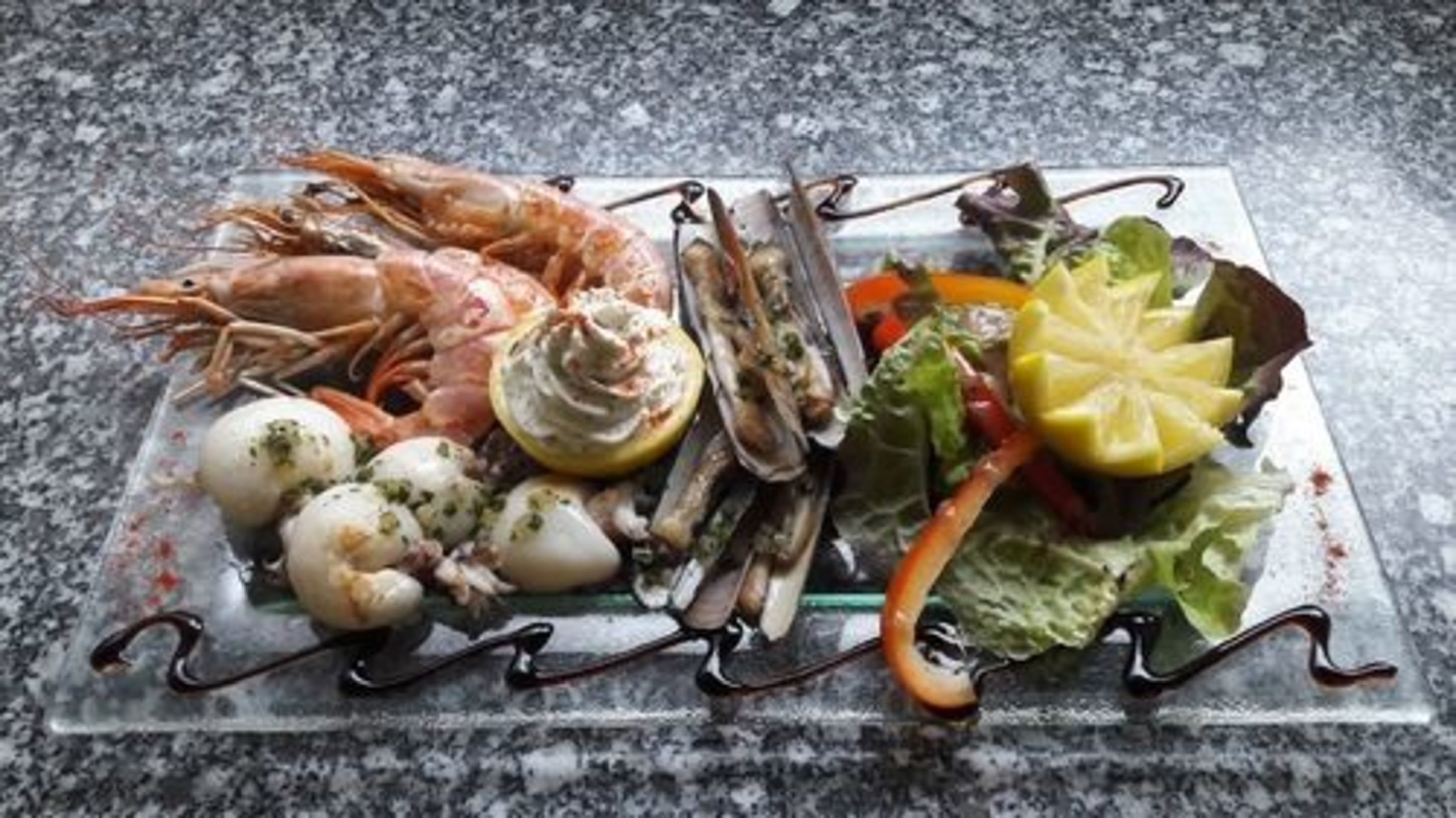 Een visplank met garnalen, kokkels en mosselen op een glazen bord.