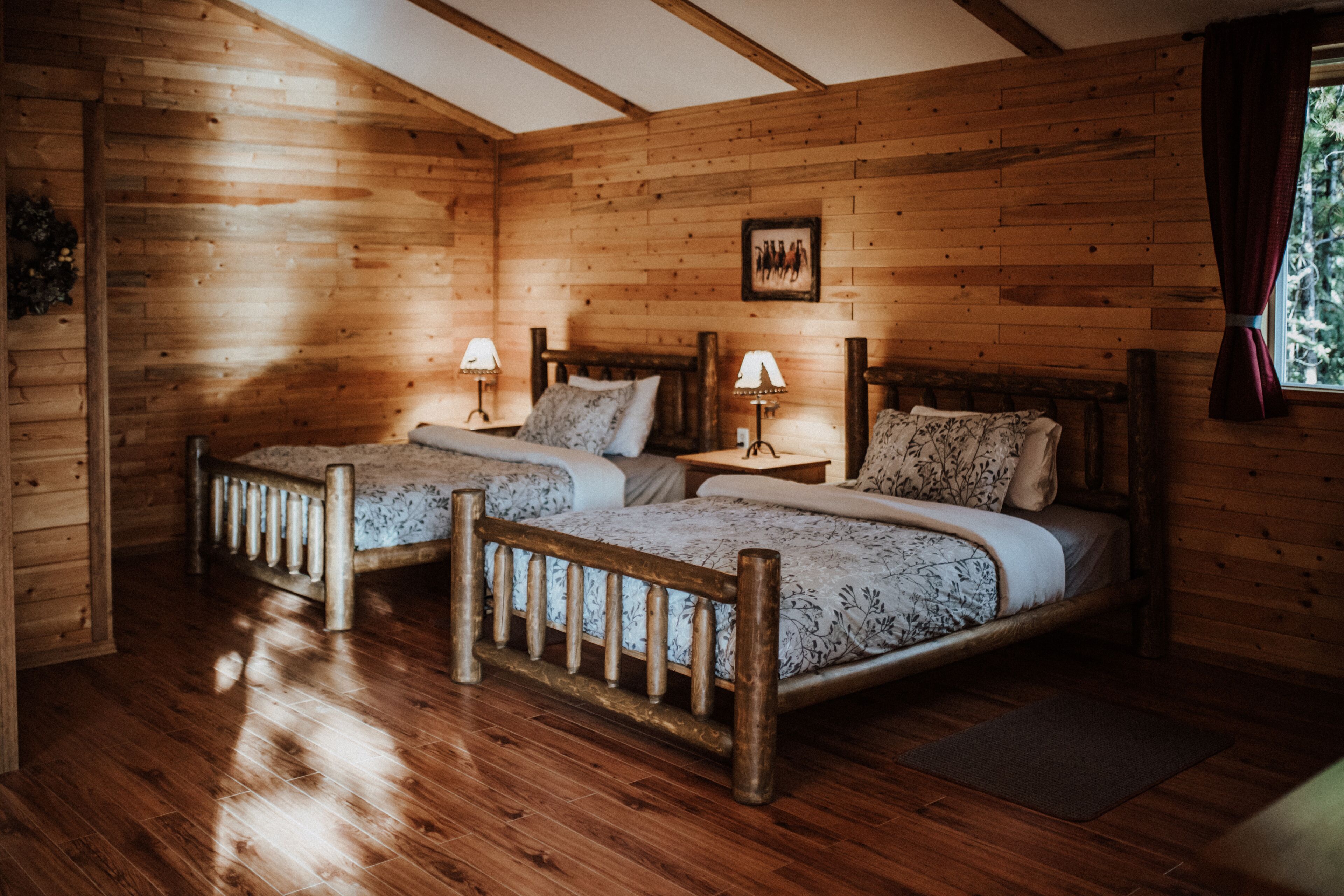 A wooden cabin bedroom with two beds, wooden floors, and a framed picture on the wall.